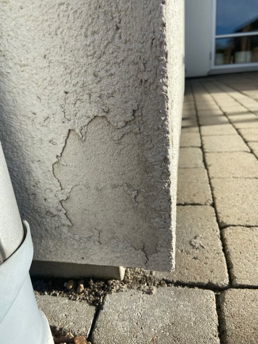 Skadad puts i hörnet av en husfasad med synlig sprickbildning och avflagning ovanför stenplattor.