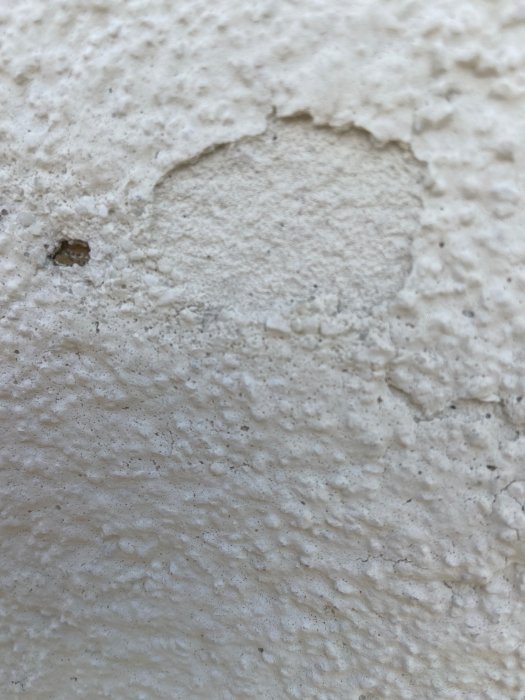 Skadat hörn på putsad fasad, visar sprucket puts och exponerad underliggande mineralskiva.