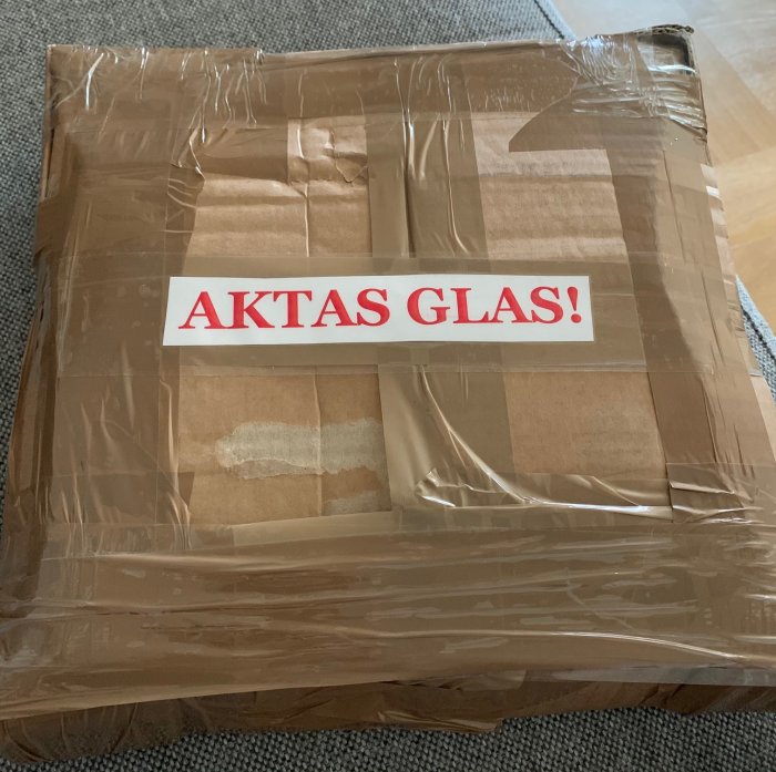 Välpackat paket med etiketten "AKTAS GLAS!" som indikerar försiktig hantering.