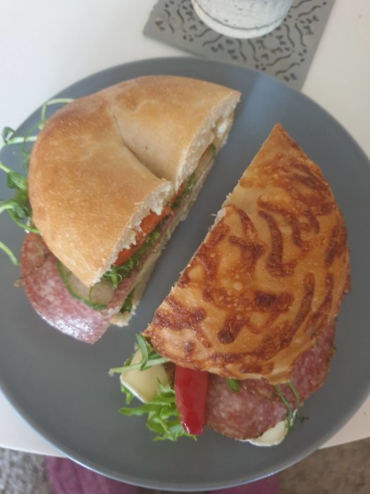 Halverad bagel med salami och brie, serverad på en grå tallrik.