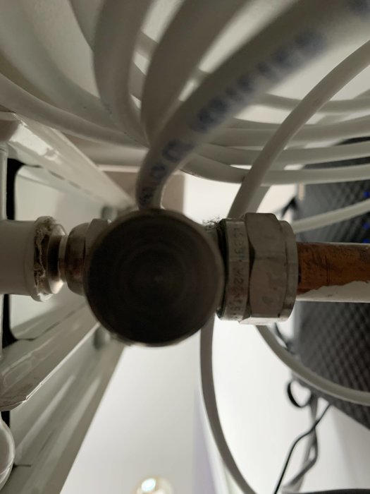 Närbild av en radiatorventil och rörkoppling med text på röret, mot suddig bakgrund.