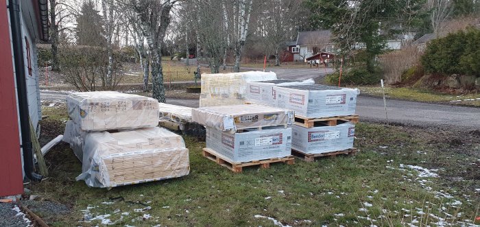 Leverans av byggmaterial perfekt packat och plastat på pallar vid en uppfart med lite snö på marken.