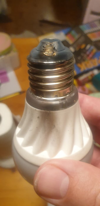 Närbild av en hand som håller en glödlampssockel med synlig varmgång och skador på kontaktpunkten.
