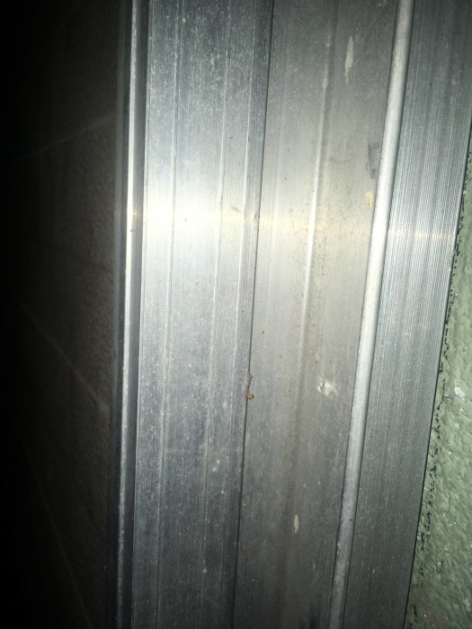 Närbild av en gammal metallskena på en port, som visar tecken på användning men inga isoleringsmaterial syns.