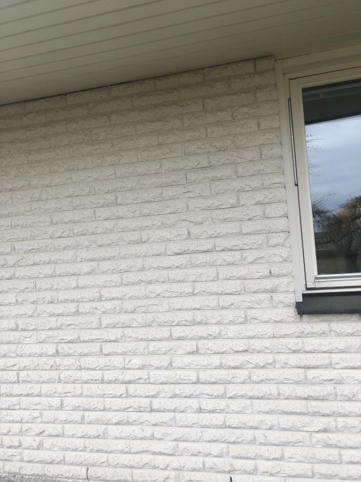 En vitmålad mexitegelvägg med ett befintligt fönster, plats för ytterligare fönsterinstallation.