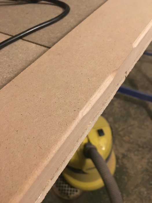 Närbild av ojämnt fräst listkant på MDF-skiva med synliga höjdförändringar.