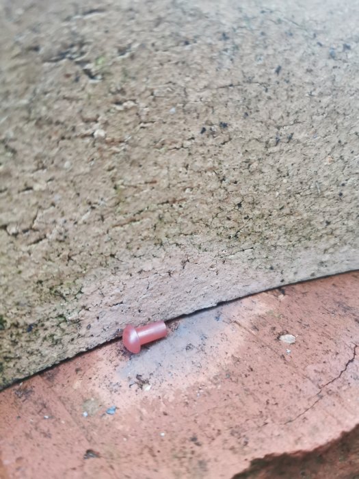 Närbild av en röd plastplugg som sitter mellan betong och tegelsten.