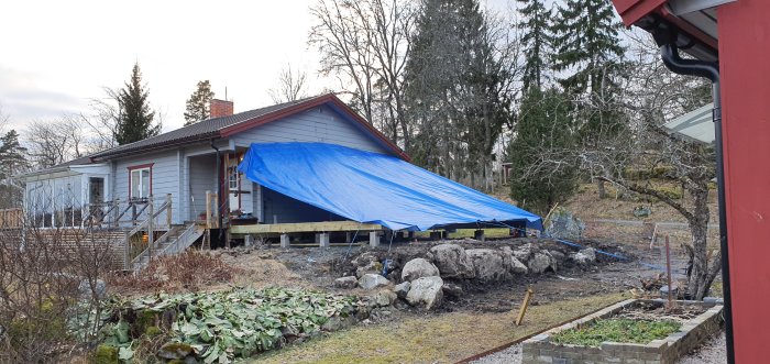 Stor blå presenning uppsatt över byggprojekt vid hus, säkrad med spännband.