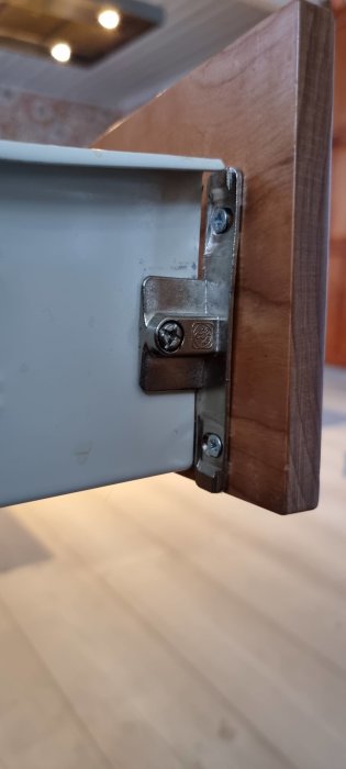Metallbeslag fastsatt vid en lådkant och träkonstruktion.