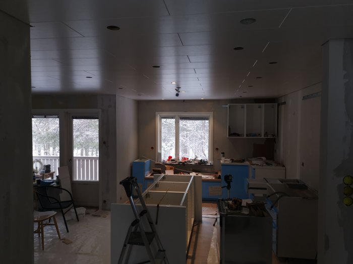 Köksrenovering i process med omonterad köksö och verktyg på golvet, synlig golvvärmeledning och vinterutsikt genom fönstret.