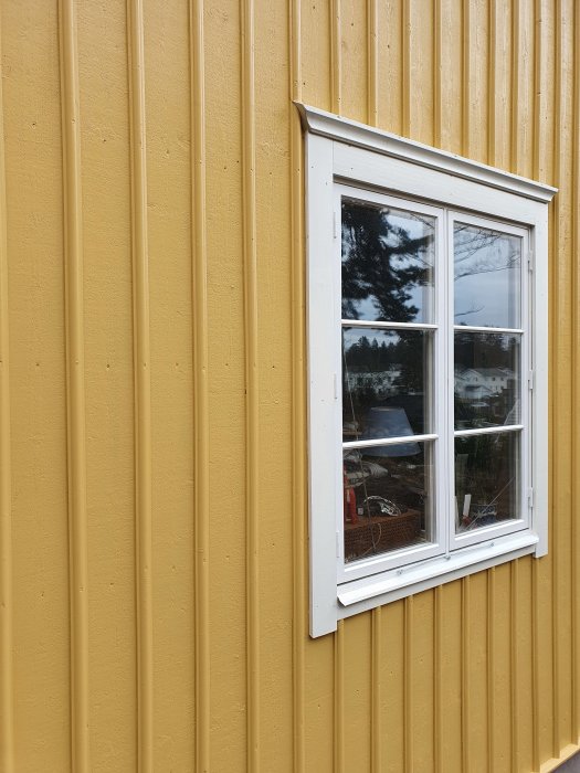 Gult stående panelhus med ett vitramat fönster utan synliga skador på panelen.