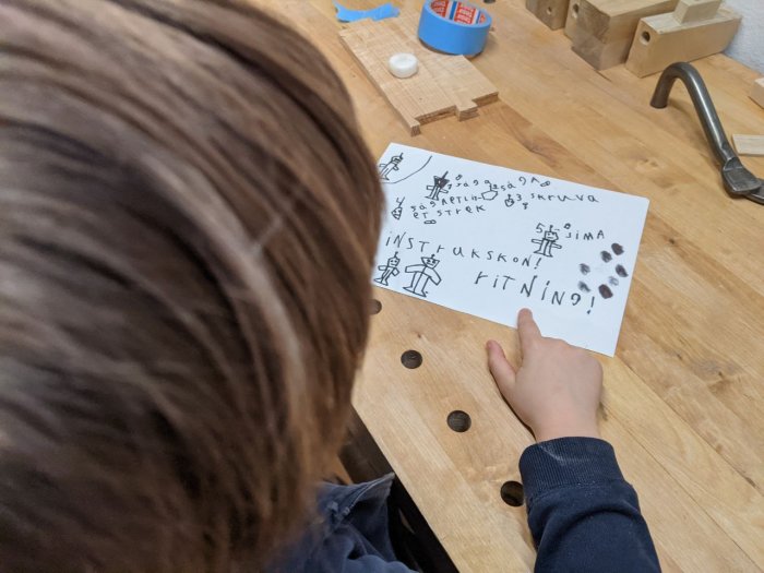 Barn pekar på handritad instruktionsritning av robotar på ett bord i ett snickeri.