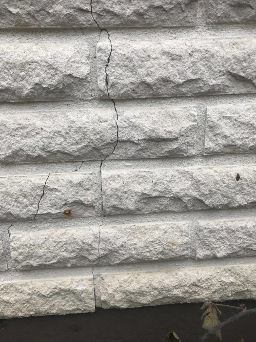 Sättningsspricka i vit mexifasadtegel, sträcker sig från grund till väggtopp.