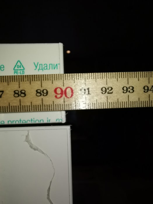 Tumstock placerad över vita skivor för att mäta bredden, visar 90 cm bredvid en sprucken kant.