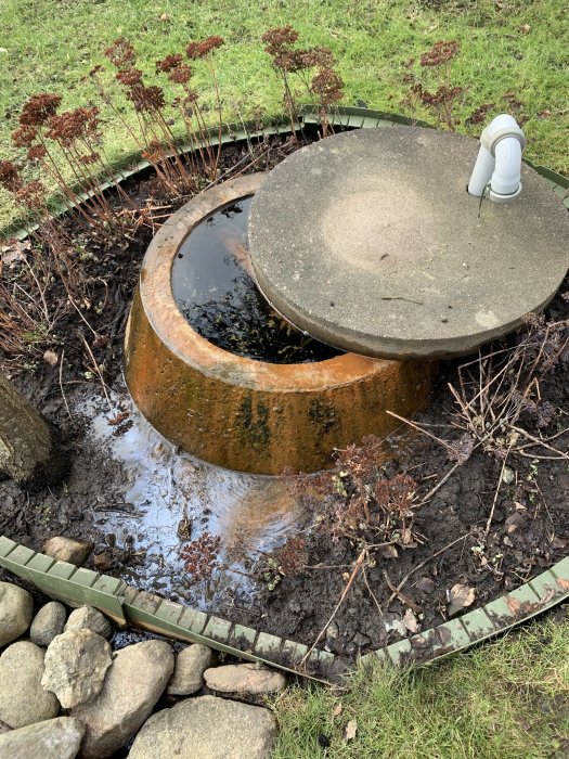 Överfylld gammal brunn på tomten med öppet lock och vatten som rinner över i gräsmattan.