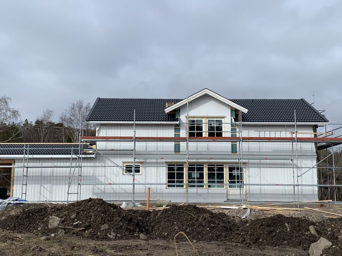 Hus under renovering med byggnadsställningar, ny målad panel och ett pågående takarbete.