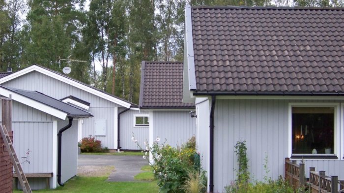 Ett vitmålat hus med PVC-panel från Kaycan och en carport, med en likadan byggnad i bakgrunden som har träpanel.