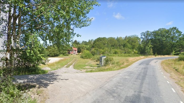 Ogrusad infartsväg som leder till rött hus med potential för anläggning av grusad allé och björkplantering.