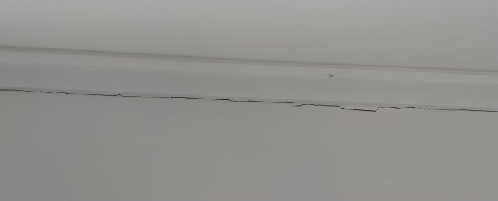 Stor spricka längs hörnet där en vit vägg möter ett vitt tak.