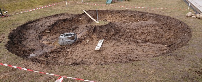 Nygrävd grop i trädgård med avspärrningsband och en skyddad brunn i mitten.