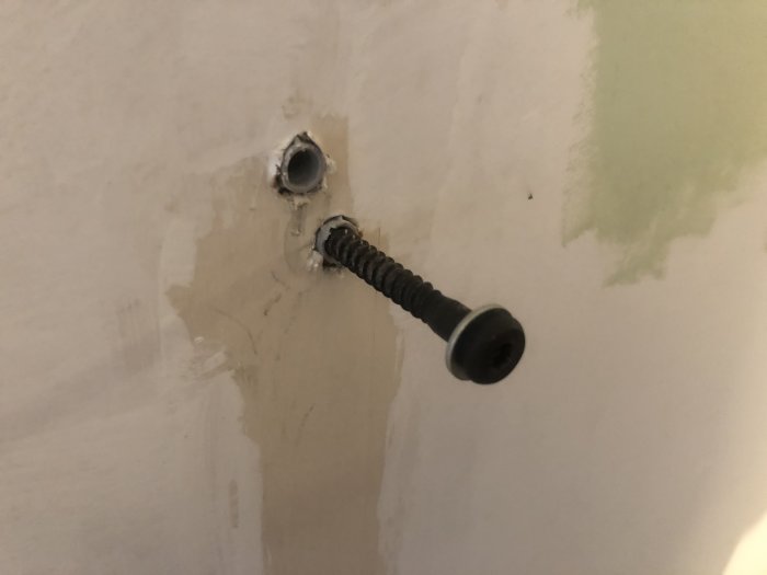 En stor plugg i en vägg med en inskruvad bult, omgiven av mindre hål och spackelspår.