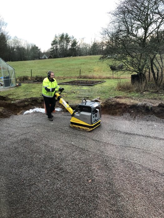 Person komprimerar makadam med en padda på en byggarbetsplats utomhus.