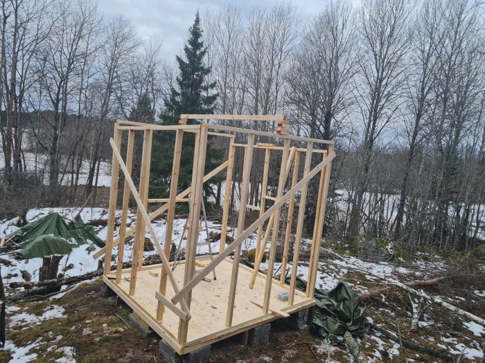 Nästan färdig trästomme av ett litet husprojekt i skogsmiljö med snöfläckar på marken.