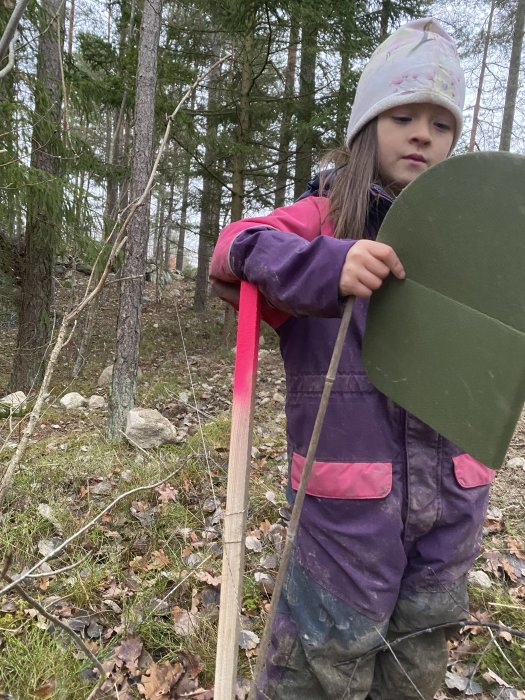 Barn markerar tomtgräns i skog med pinne och rosa snöre.