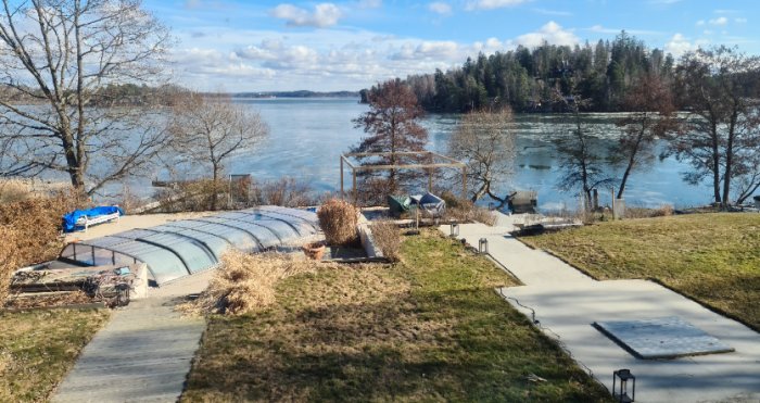 En välplanerad trädgård med en nyanlagd betonggång och en altan med utsikt över en lugn sjö och skog i bakgrunden.