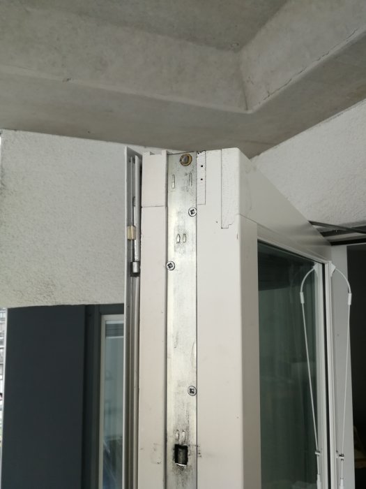 Övre delen av en dörrkarm med synlig dörrbromsmekanism och delvis öppen dörr på en balkong.