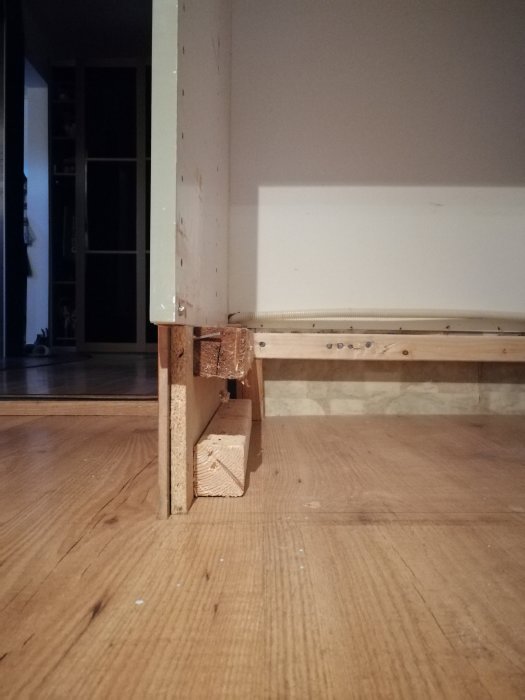 Köksskåps botten som kapats för att passa en diskmaskin med avskurna reglar och spånskiva mot ett trägolv.