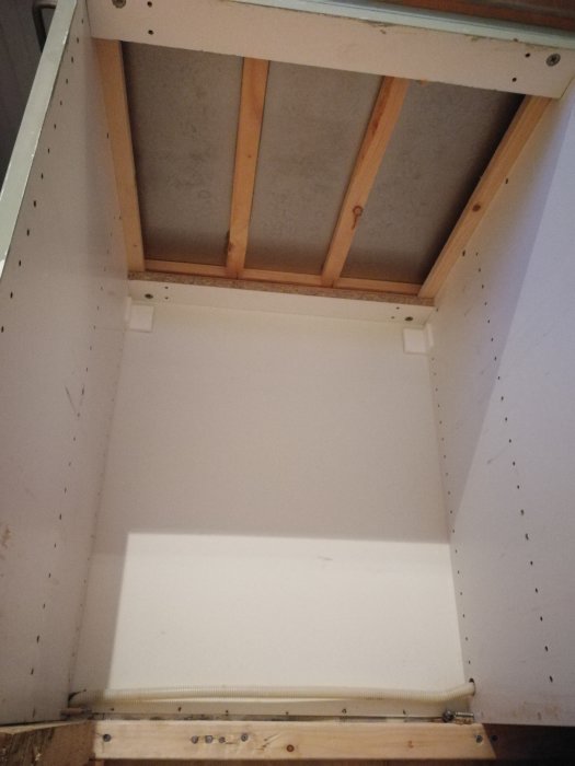 Utrymme under en köksbänk med kapade reglar och en spånskivabotten.