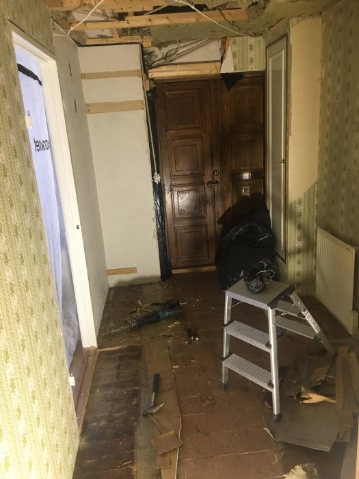 Renoverad hall med upptaget parkettgolv som avslöjar underliggande kork, gammalt trägolv och byggavfall.