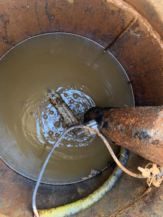 Tömd brunn med lösa elkablar, kopplingsklämmor och ett järnrör med vajer över stort rör ner i marken.