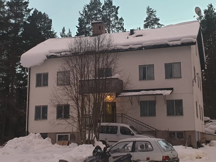 Hyresfastighet med fyra lägenheter täckt av snö, i behov av renovering med synliga fönster och fordon framför.