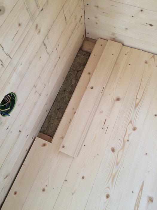 Nyinstallerade trägolvbrädor monterade vid en hörnkant i ett rum, med den sista plankan lagt på plats.