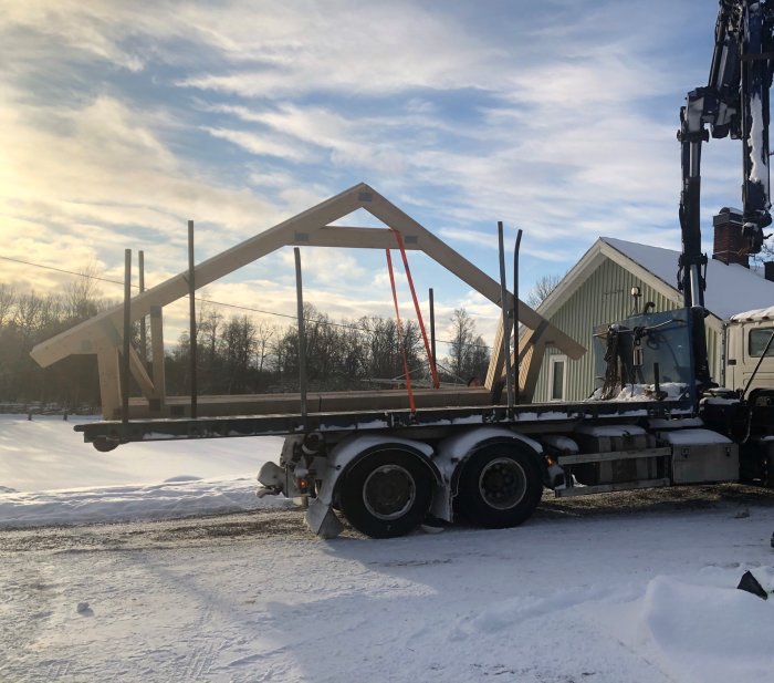 Lastbil med byggkran lyfter prefabrikerade trästommar på en snötäckt byggplats.