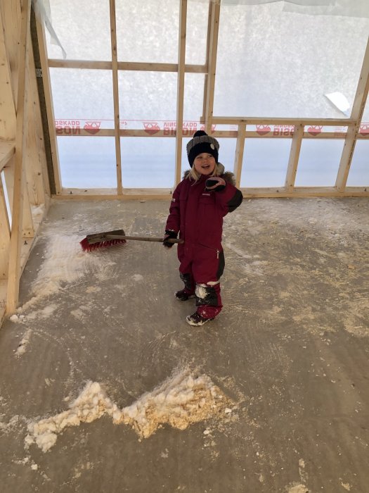 Barn som sopar bort pudersnö inuti stommen till ett hus under uppbyggnad.