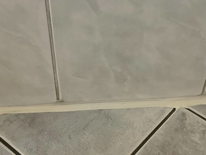 Närbild av grå kakelfog vid golv, nyligen bytt och utan svärta i kanterna.