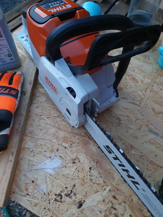 Stihl MSA 220 batterisåg på spånskiva med handske och sågspån i bakgrunden, använd för träarbete.