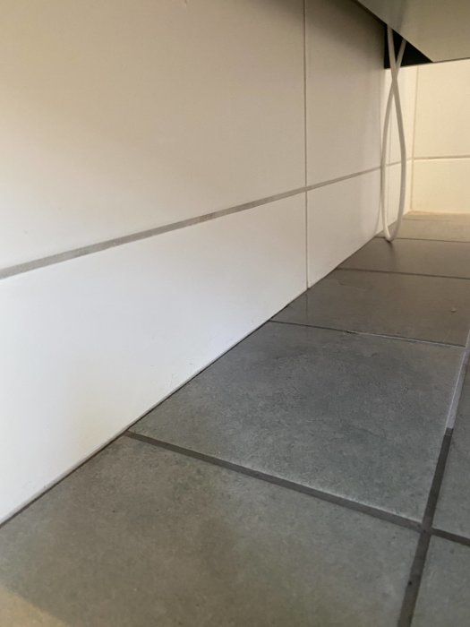 Vattenläckage vid rörgenomföring bakom badrumskommod på en grå kaklad golv.