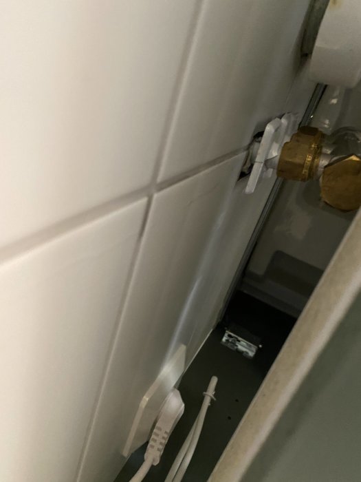 Läckande vatten från hål i vägg vid badrumskommod med synliga rör och kablar.