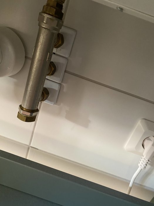 Vattenläcka bakom handfatet med synligt rör och hål i väggen där ledningen går ut.