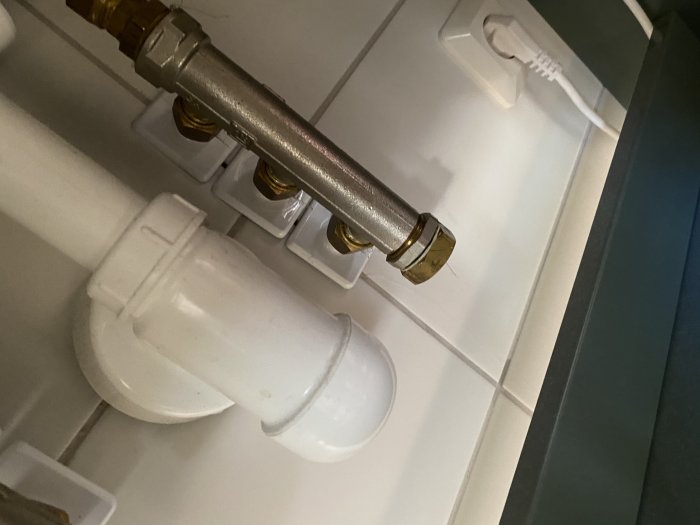 Vattenledningsrör och avloppsrör synliga bakom badrumskommoden, möjlig läckagepunkt vid väggen.