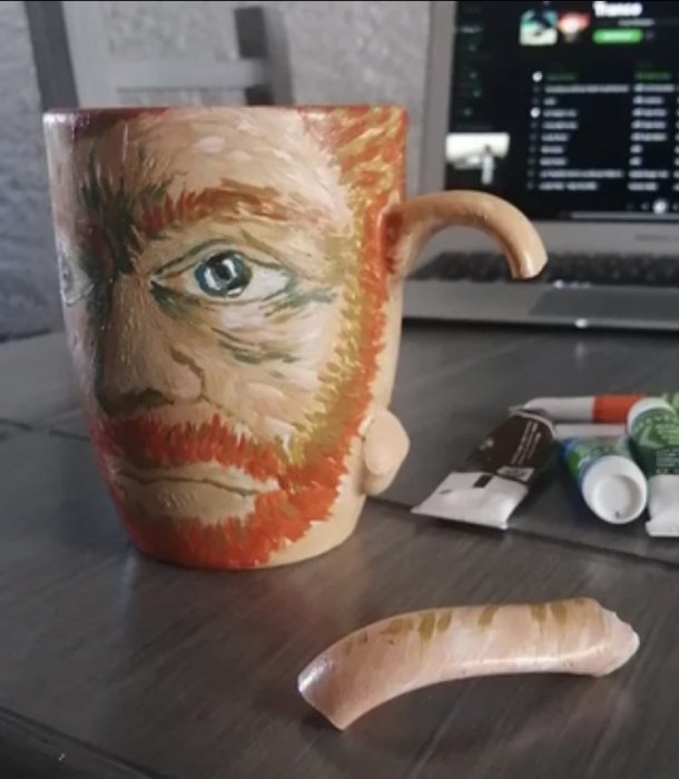 Mugg med ansiktsdesign och bruten handtag som liknar en näsa på ett bord.