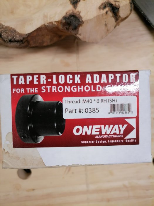 Låda för TAPER-LOCK ADAPTOR från ONEWAY med specifikation M40 gänga, delnummer 0385 framför trästycke.