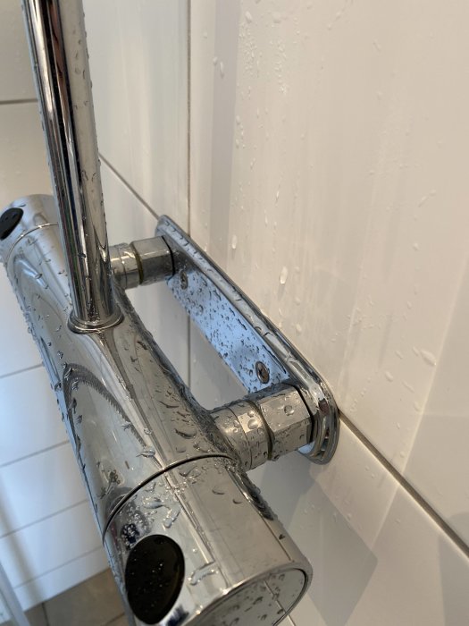 Kromad duschblandare med vattendroppar mot en kaklad vit vägg.