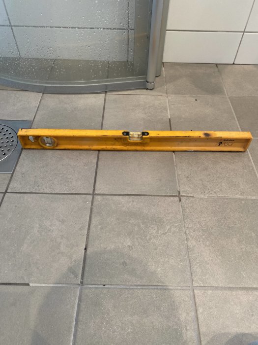 Vattenpass på klinkergolv med duschhörn i bakgrunden, kontrollerar golvets lutning.