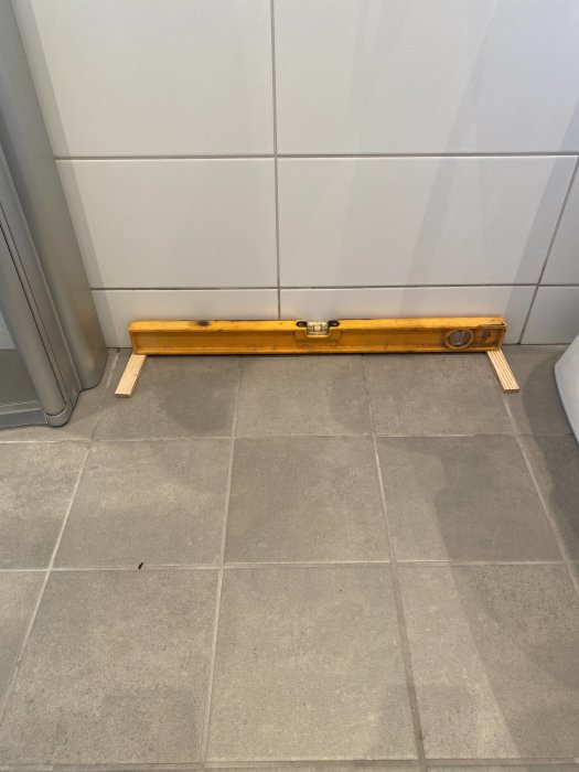 Vattenpass på ett kaklat golv visar fel lutning vid väggen.