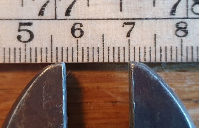 Skiftnyckelns käftar framför måttband som visar mått i centimeter på ett träbord.